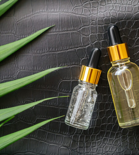 Collagen Serum or hyaluronic serum in dropper on black color crocodile skin texture background with palm leaves. Skincare cosmetic product bottle. Cosmetics health face skin beauty.